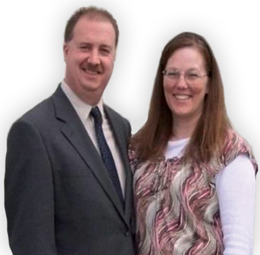 Middle aged balding white man with a mustache in a suit standing next to long haired woman with glasses, both smiling